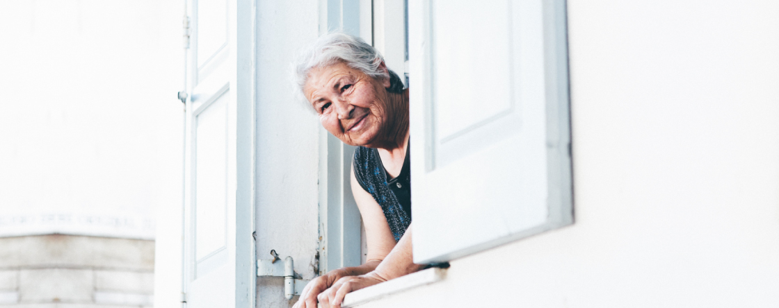 Mujer adulta mayor cuidadora mirando por ventana feliz